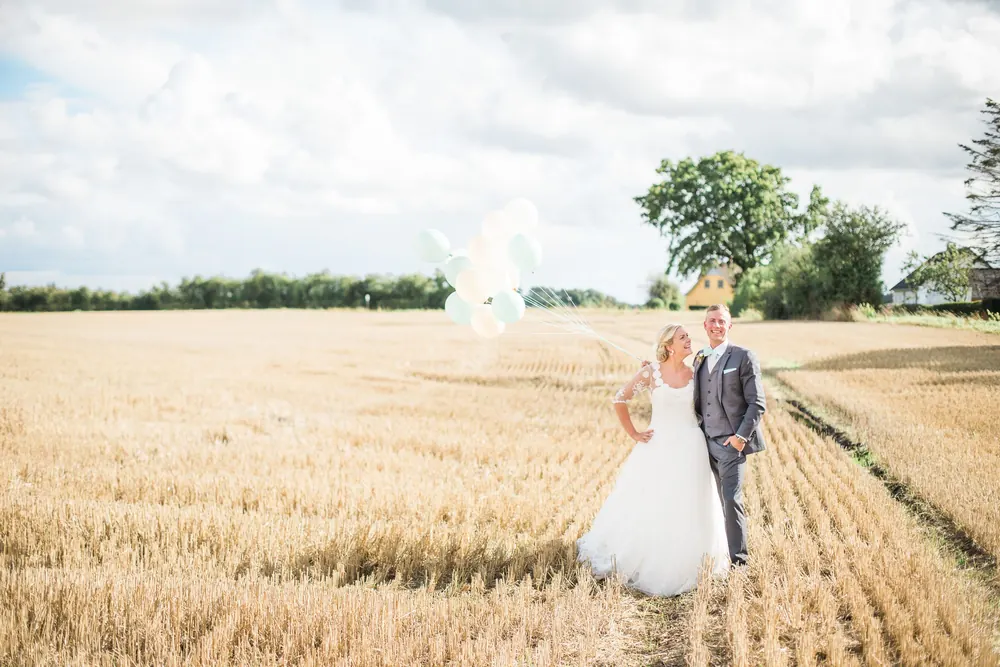 Bride and groom laughing together in a wheat field with balloons